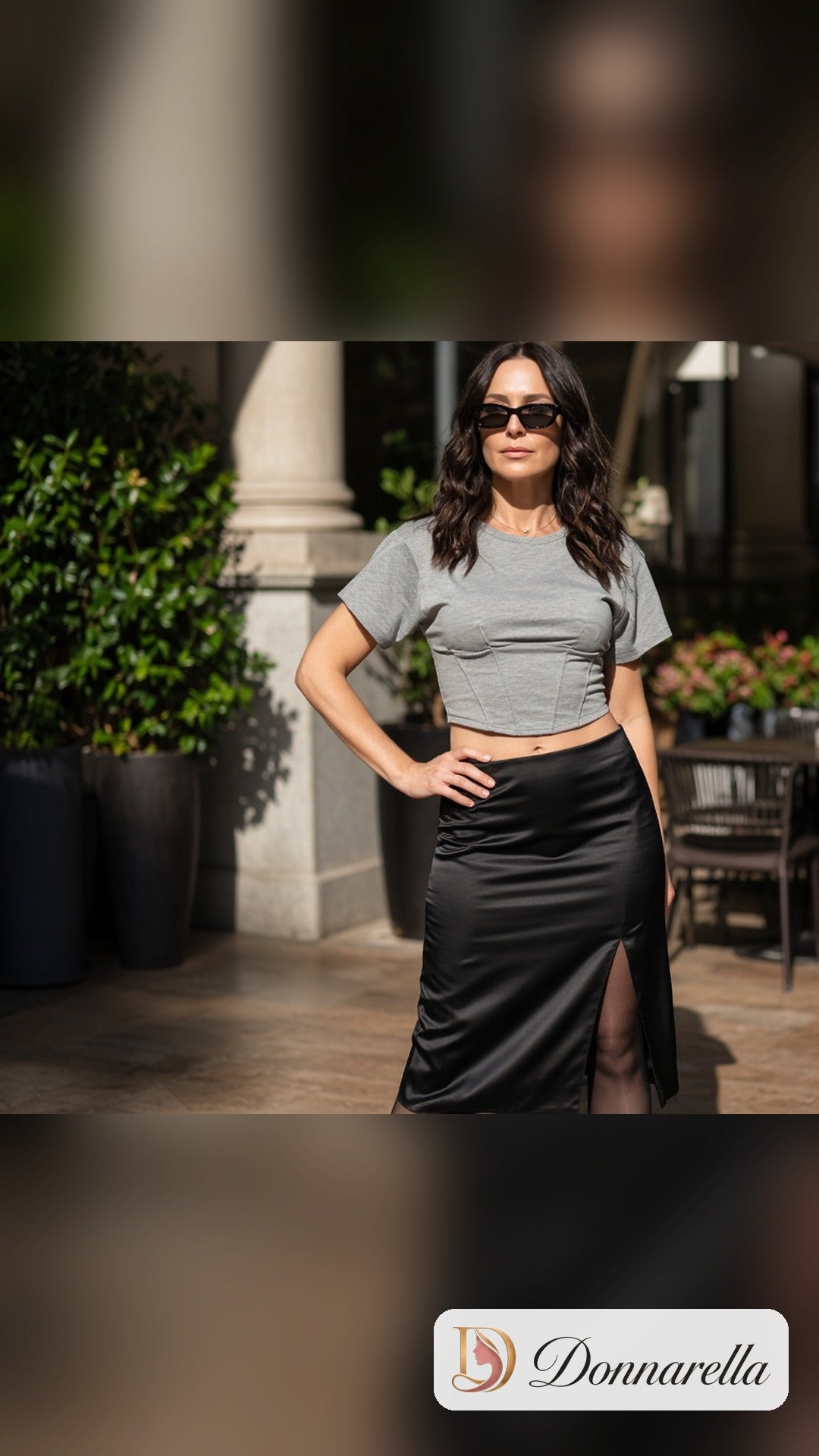 Modelo da Donnarella usando a Camiseta Cropped Feminina Cinza Estilo Corset com saia midi preta de cetim e óculos escuros